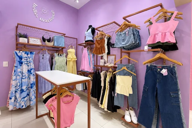 Cantinho da Hello Maricota na loja, com parede lilás e moda juvenil